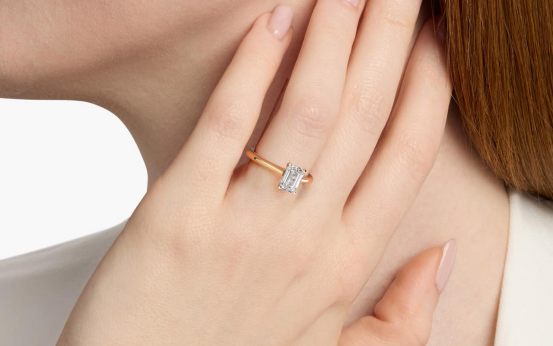 Hand wearing a vintage-style two-tone engagement ring with an emerald-cut lab grown diamond.