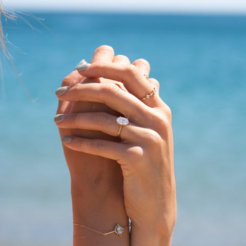 Couple’s hands clasped at the beach, featuring an oval-cut lab grown diamond ring styled to elongate the fingers.