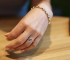 Hand wearing an emerald-cut lab grown diamond ring with a halo setting, styled casually on a wooden table.