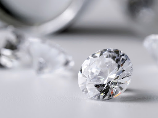 Polished cushion-cut lab grown diamond on a light grey surface, illustrating the stone to be cleaned in a care guide.