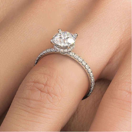 Close-up of a hand wearing a halo-style engagement ring featuring a lab grown diamond center stone, set in a pavé band.