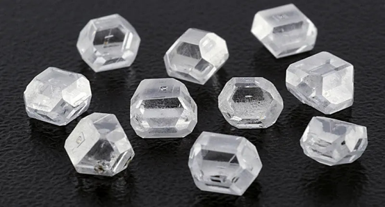 Rough, uncut lab grown diamond crystals scattered on a black surface, representing the initial stage of diamond production.