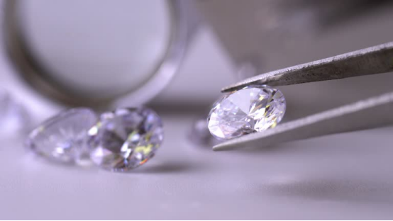 Oval-cut lab grown diamonds being examined with tweezers, set against a jeweler’s work surface, for a 0.32 vs 0.35 carat comparison.